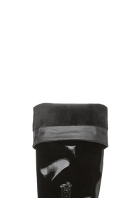 Bota negra hasta la rodilla con acabado en charol y un puño de ante negro aterciopelado, que presenta una textura suave y un diseño minimalista.