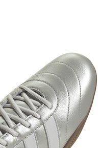 Scarpa atletica in pelle argento con tomaia testurizzata, chiusura con lacci e suola in gomma. Caratterizzata da tre strisce bianche sul lato.