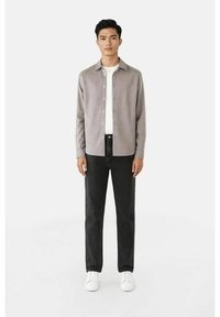 Lys grå button-up skjorte over en hvit T-skjorte, parret med svarte jeans og hvite sneakers. Slim fit, myk tekstur og klassisk design.