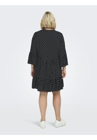 Schwarzes Kleid mit weißen Punkten, ausgestellten Ärmeln und einem Rüschenabschluss. Hergestellt aus weichem Material, hat es einen runden Ausschnitt und eine lockere Passform.