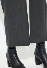 Upravené šedé kalhoty s rovnou nohavicí, které mají jemnou strukturu. Spárovány s elegantními černými koženými botami na podpatku s přiléhavým designem kolem kotníku.