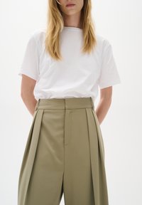 Vit t-shirt med kort ärm i kombination med högmidjade olivgröna veckade byxor. Slätt tyg med en ren, enkel design. Minimalistisk stil.