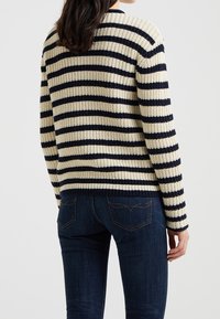 Pull en maille à rayures horizontales crème et marine, col rond, manches et ourlet côtelés, associé à un jean en denim foncé.