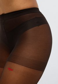 Διαφανέστερες μαύρες καλτσοδέτες με απαλή υφή, με αντίθετη κόκκινη κεντητή λεπτομέρεια με χείλος στο μηρό. Περιλαμβάνεται ελαστική ζώνη μέσης.