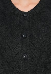 Svart strikket cardigan med V-halsdesign, med et teksturert mønster og tre svarte knapper foran.