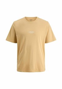 T-shirt à manches courtes beige clair en coton doux, avec un col rond et un logo discret "JJ Studios" blanc sur la poitrine.
