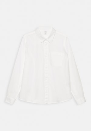 Biała koszula z długim rękawem wykonana z gładkiej tkaniny, z zapięciem na guziki z przodu, kołnierzykiem z wąskimi szpicami oraz kieszenią na lewej piersi.