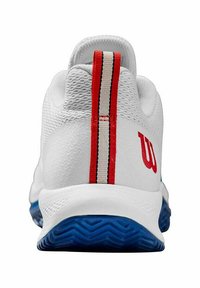 Zapatilla de tenis con una parte superior de malla blanca, una franja vertical roja y blanca en el talón, y una suela de goma azul con un patrón en zigzag.