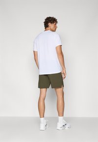 T-shirt branca de manga curta, com decote redondo, combinada com calções verdes escuros. Modelo a usar ténis brancos e meias brancas até ao tornozelo, vista por trás.