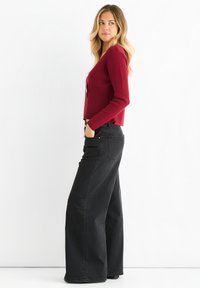 Maglione fitted borgogna abbinato a jeans neri a gamba larga con vita alta. Il maglione ha un colletto a V e una texture a coste, i pantaloni hanno tasche.