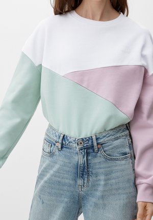 Femme portant un sweat-shirt bicolore blanc, vert menthe et violet clair, associé à un jean taille haute bleu clair.