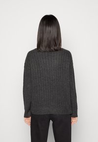 Pull en maille côtelée gris foncé avec une coupe ample, des épaules tombantes et des manches longues, porté avec un pantalon noir.