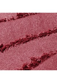 Gros plan de poudre d’ombre à paupières rose scintillante écrasée avec des stries texturées à la surface.