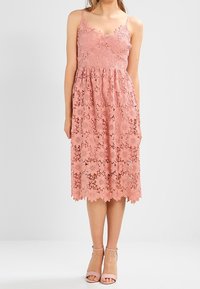 Robe en dentelle rose avec un corsage ajusté, un décolleté festonné et une jupe évasée. Présente des motifs floraux et un ourlet avec des bords festonnés.