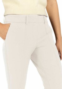 Tailored light beige pants with a smooth texture. Features a straight fit, side pockets, and clean lines for a structured look.