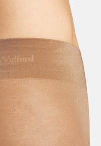 Genomskinliga bruna strumpbyxor med en bred, ribbad midja som har varumärket "Wolford" tryckt i en subtil, ton-i-ton design. Slät och elastisk material.