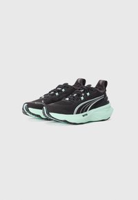 Une paire de baskets de sport noires et vert menthe avec des semelles épaisses, des tiges en mesh et des logos Puma réfléchissants sur un fond blanc.