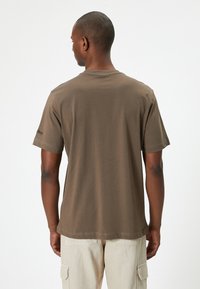 Brun kortærmet T-shirt lavet af bomuld, med rund hals, lige kant og et diskret logo på venstre ærme.
