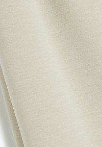 Beige stof met een gladde textuur, met een subtiel weefpatroon. Het valt soepel, waardoor licht en schaduw over het oppervlak heen spelen.