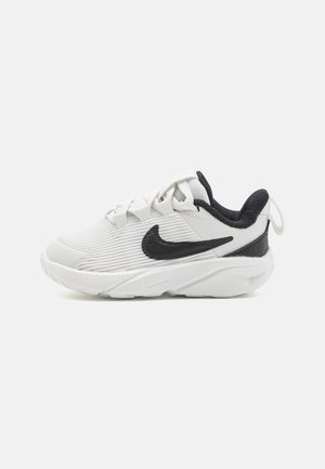 Zapatilla Nike en blanco y negro con tejido texturizado, logo Swoosh negro, cordones blancos y suela gruesa y acolchada, vista de lado sobre fondo blanco.