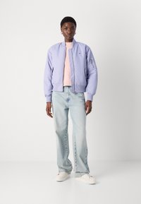 Ljubičasta bomber jakna s rebrastim manžetama i ovratnikom, nošena preko svijetlo ružičaste pletene majice. Uparena s laganim plavim širokim trapericama i bijelim tenisicama.