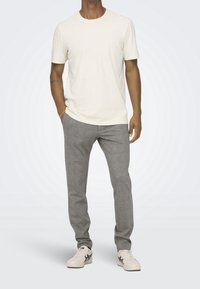 Camiseta de cuello redondo gris claro y pantalones a cuadros grises. El modelo lleva zapatillas blancas con detalles en azul marino. Tela suave, diseño ajustado.