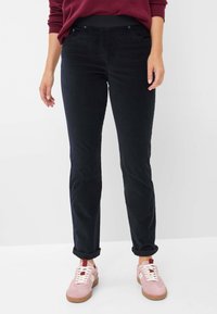 Zwarte corduroy broek met een slim fit, voorzien van voorzakken en opgerolde mouwen, gecombineerd met lichtroze sneakers en witte veters.
