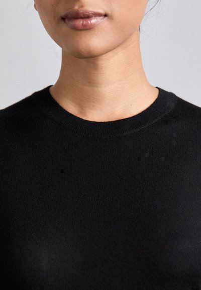 Black knit sweater with a round neckline, featuring a smooth texture and close-fitting design, focusing on a minimalist aesthetic.