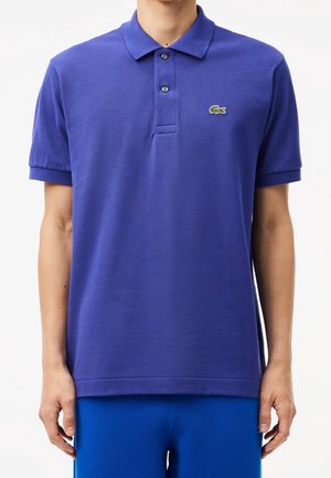 Lila Poloshirt aus strukturiertem Stoff, mit Kragen, Drei-Knopf-Leiste und kleinem grünem Krokodil-Logo auf der linken Brust.