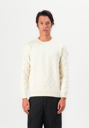 Suéter crema claro con patrón geométrico texturizado, cuello redondo y puños acanalados; combinado con pantalones cargo negros.