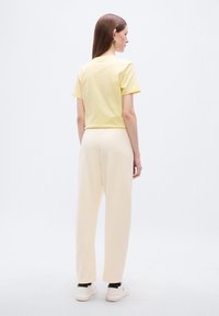 Κίτρινη βαμβακερή μπλούζα σετ με απαλό, ανοιχτό χρωματικά κρεμ παντελόνι με φαρδιά πόδια. Το σύνολο ολοκληρώνεται με λευκά αθλητικά παπούτσια με μαύρες λεπτομέρειες.