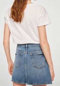 Witte katoenen t-shirt gecombineerd met een strakke blauwe denim minirok. De rok heeft achterzakken en een hoge taille.
