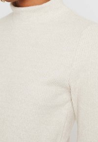 Hochgeschnittener, gerippt gestrickter Oberteil in Off-White, der eine weiche Textur und eine figurbetonte Passform zeigt, mit einem nahtlosen, sauberen Finish.