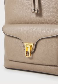 Borsa in pelle beige textured con chiusura a pattina, dotata di una serratura in metallo dorato e dettagli in metallo. Finitura liscia con bordi scuri a contrasto.