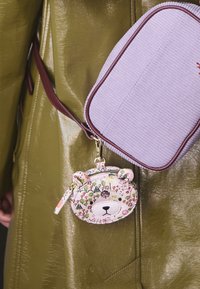 Pasztell színű virágmintás maci formájú érmepénztárca cipzáras záródással és fül díszítéssel, egy barna szegélyű levendula színű bordázott válltáskához rögzítve.