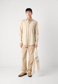 Cămașă bej cu guler, pantaloni bej și geantă de umăr bej. Material neted, croi normal, cu guler și mâneci lungi. Cizme din suede.