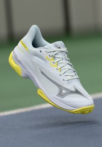 Lightweight tennis shoe in white with yellow accents. Features a textured upper, lace closure, and a durable rubber outsole designed for court traction.