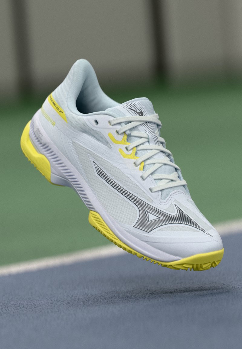 Lightweight tennis shoe in white with yellow accents. Features a textured upper, lace closure, and a durable rubber outsole designed for court traction.