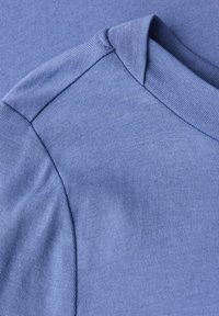 Gros plan sur un tissu tricoté bleu clair montrant la couture de l'épaule et le col replié d'un vêtement.