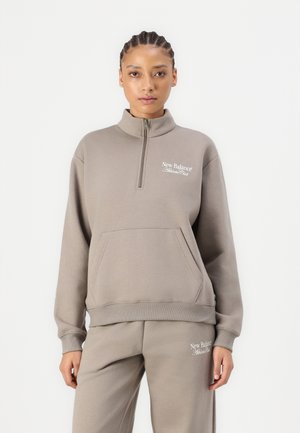 Felpa grigia con zip, collare alto e tasca frontale. Presenta il logo "New Balance Athletic Club" in bianco. Tessuto morbido, design casual.