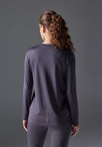 Långärmad träningströja i mörklila, med en slät textur och subtil reflekterande detalj på baksidan. Kombinerad med matchande leggings.