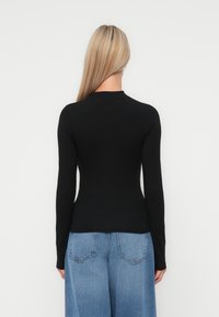 Black long-sleeve top with a high neckline and fitted shape. Paired with light blue wide-leg denim jeans featuring back pockets.