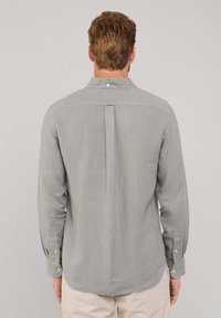 Maglietta a maniche lunghe grigio chiaro in misto lino, con colletto con bottoni, piega singola sul retro e polsini con bottoni. Tessuto liscio, vestibilità casual.
