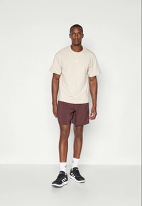 Beige treningsgenser med korte ermer, maroon shorts og svarte joggesko. Hvite detaljer på skoene og logoen på genseren.