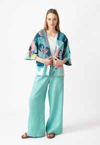 Spalvinga, raštuota kimono stiliaus striukė mėlynos, rožinės ir žalios spalvos, dėvima ant balto viršaus, derinama su šviesiai akvamarino spalvos platėjančiais kelniais.