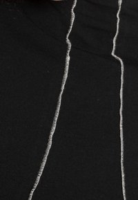 Svart tygblus med två kontrasterande grå vertikala sömmar fram, som skapar en texturerad linjedetalj. Mjuk bomullsmaterial.