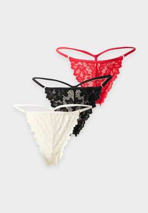 Trois strings en dentelle de couleurs blanche, noire et rouge, disposés sur un fond gris clair.
