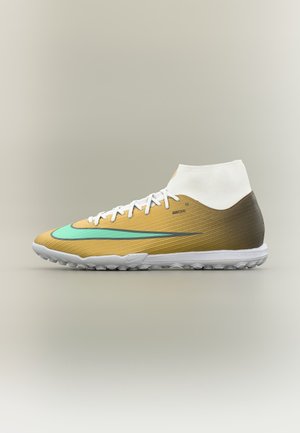 Scarpa da calcio Nike alta dorata e bianca con swoosh turchese e suola testurizzata, progettata per campi in erba sintetica o per il gioco indoor.