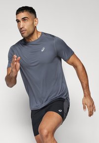 Athletisches kurzärmeliges Shirt in Dunkelgrau, aus leichtem Material gefertigt, mit rundem Ausschnitt und einem Logo auf der Brust, kombiniert mit schwarzen Shorts.