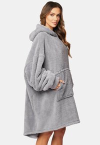 Sudadera de felpa gris de gran tamaño con un gran bolsillo delantero y mangas anchas. Textura suave y capucha redondeada. El dobladillo es ligeramente más largo en la parte posterior.